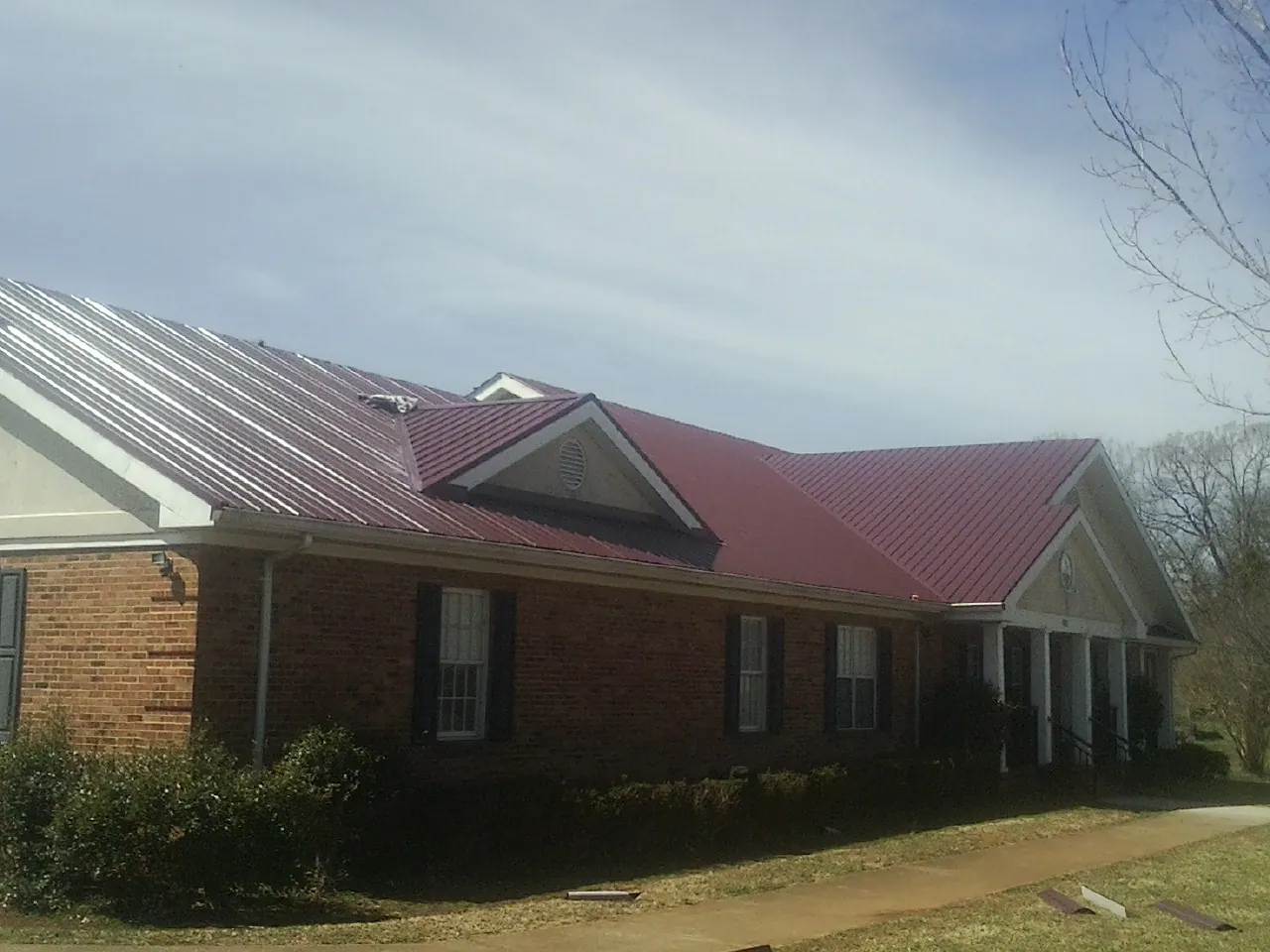 Red metal roof with gabled entries on a long brick building, from a Hail Damage Roof Repair job in Imler
