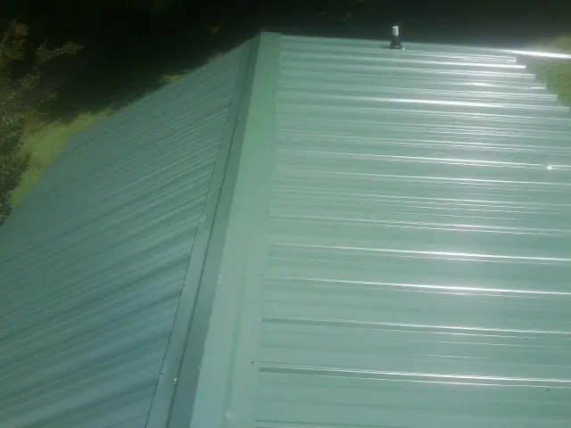 New green metal panels meeting at the ridge of a roof — Flat Roof Repair work by our crew in Imler