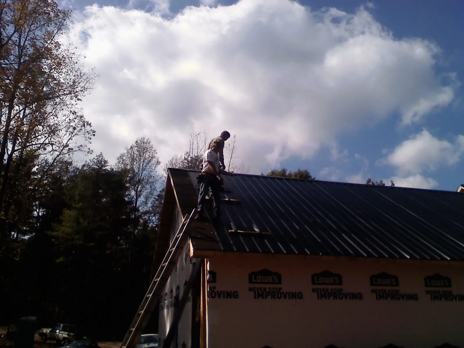 Roofer fastening dark metal panels high against a cloudy sky, from a Roof Inspection job in Imler